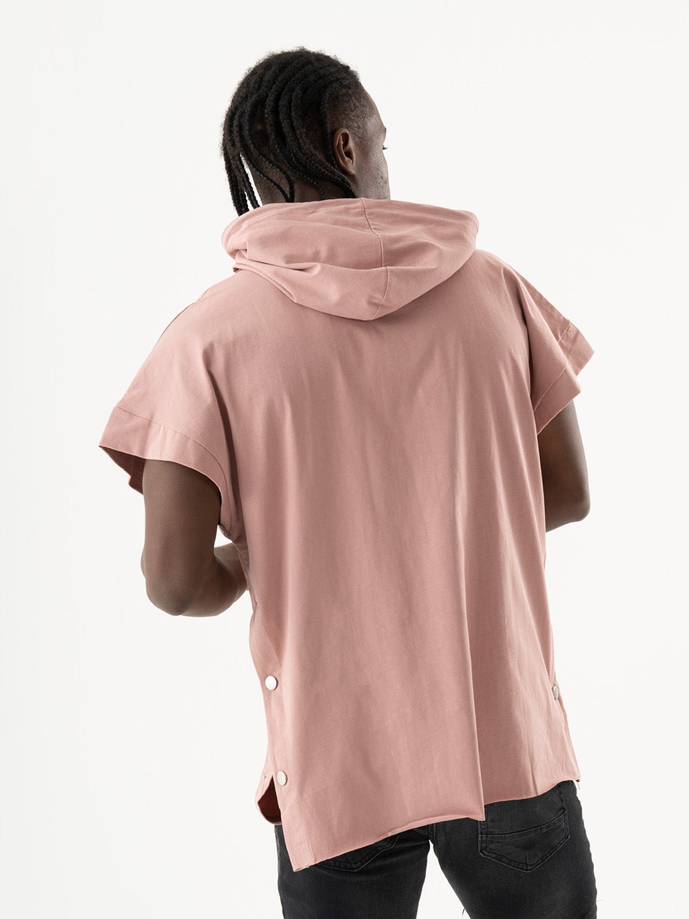 A person with braided hair wearing a salmon RIGGED HOODIE, standing with their back to the camera.